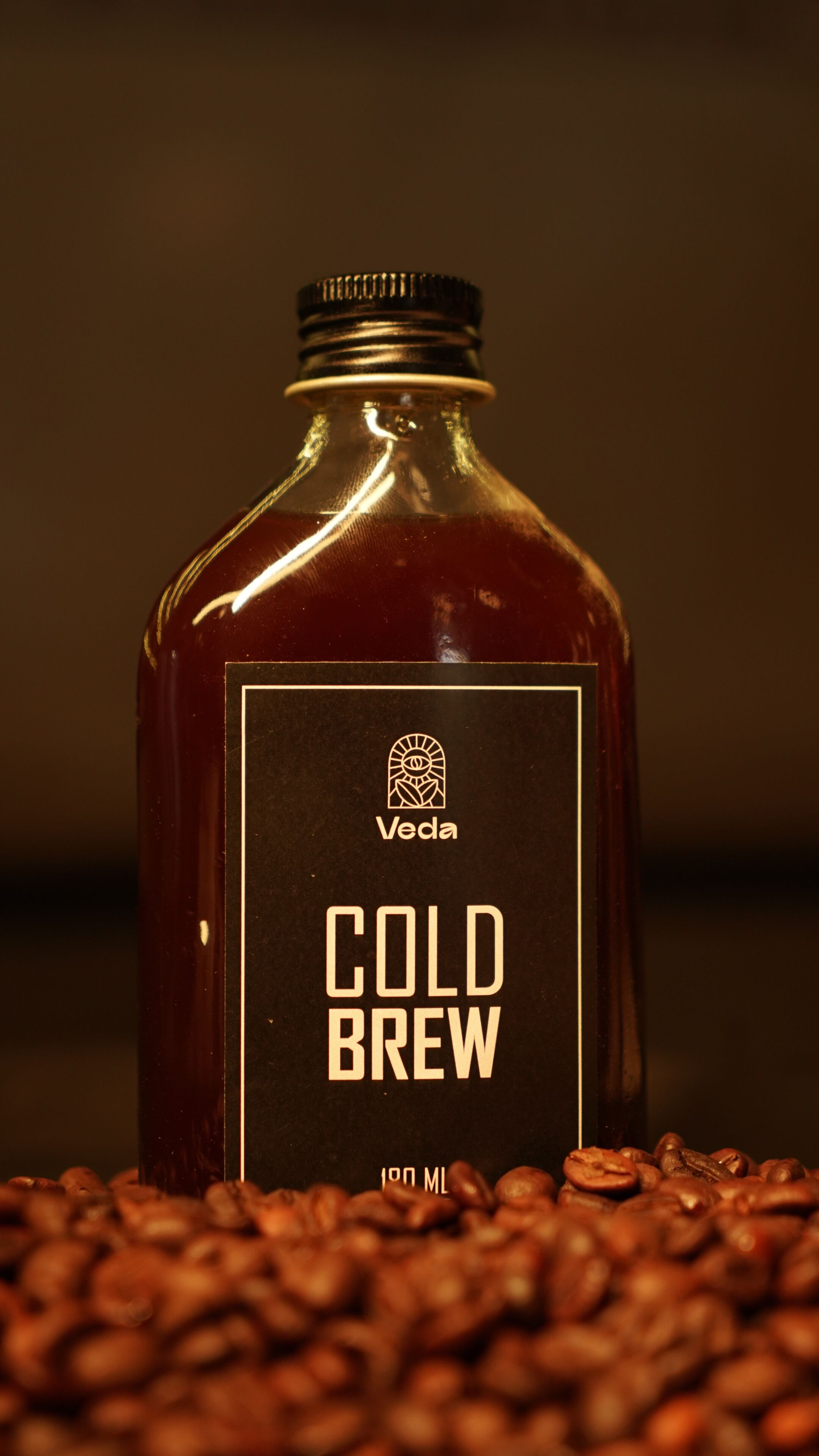 Una botella de Veda Cold Brew con etiqueta, rodeada de granos de café.
