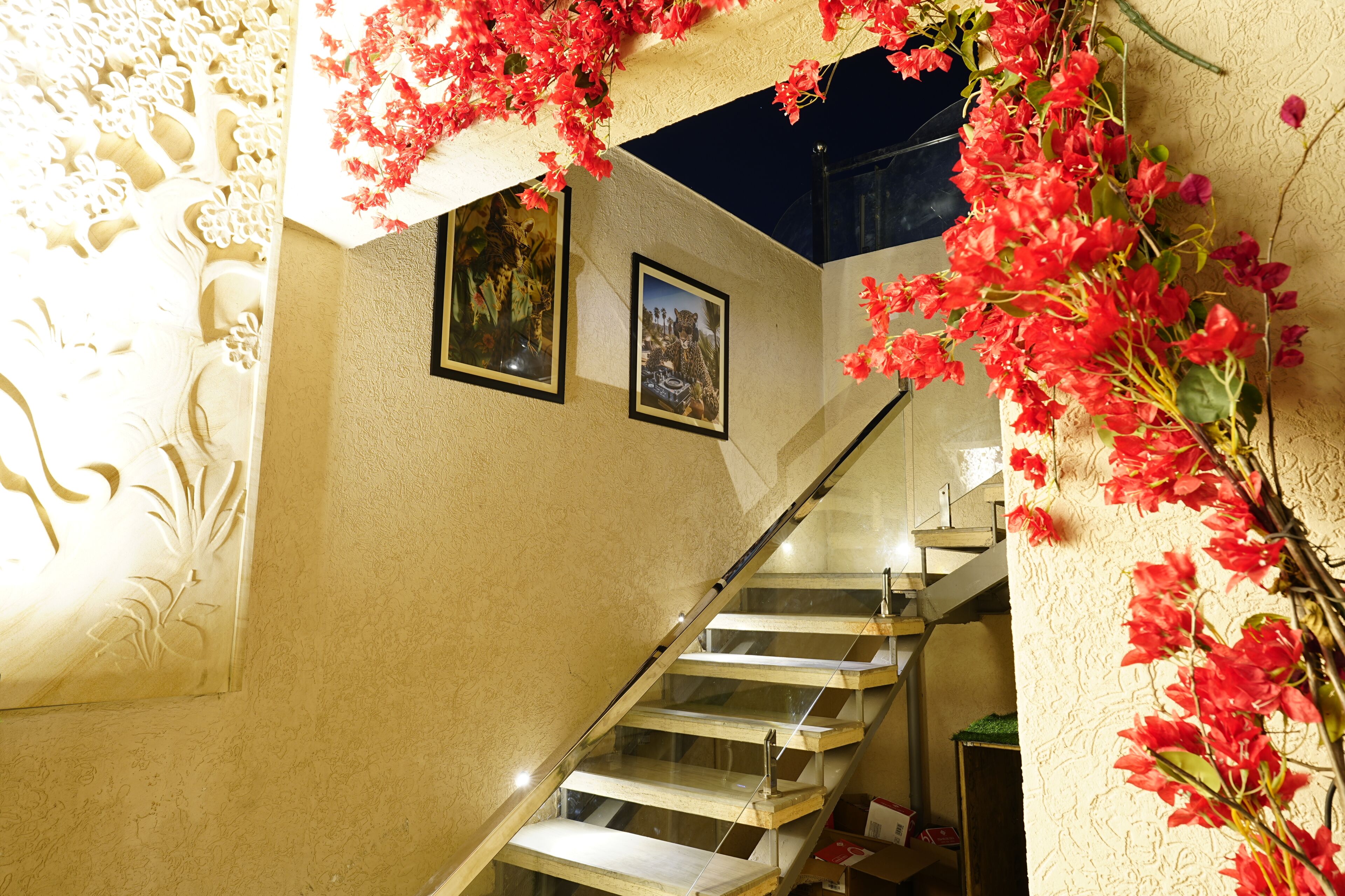 Una escalera con barandillas de cristal, una pared con detalles florales tallados y dos cuadros enmarcados.
