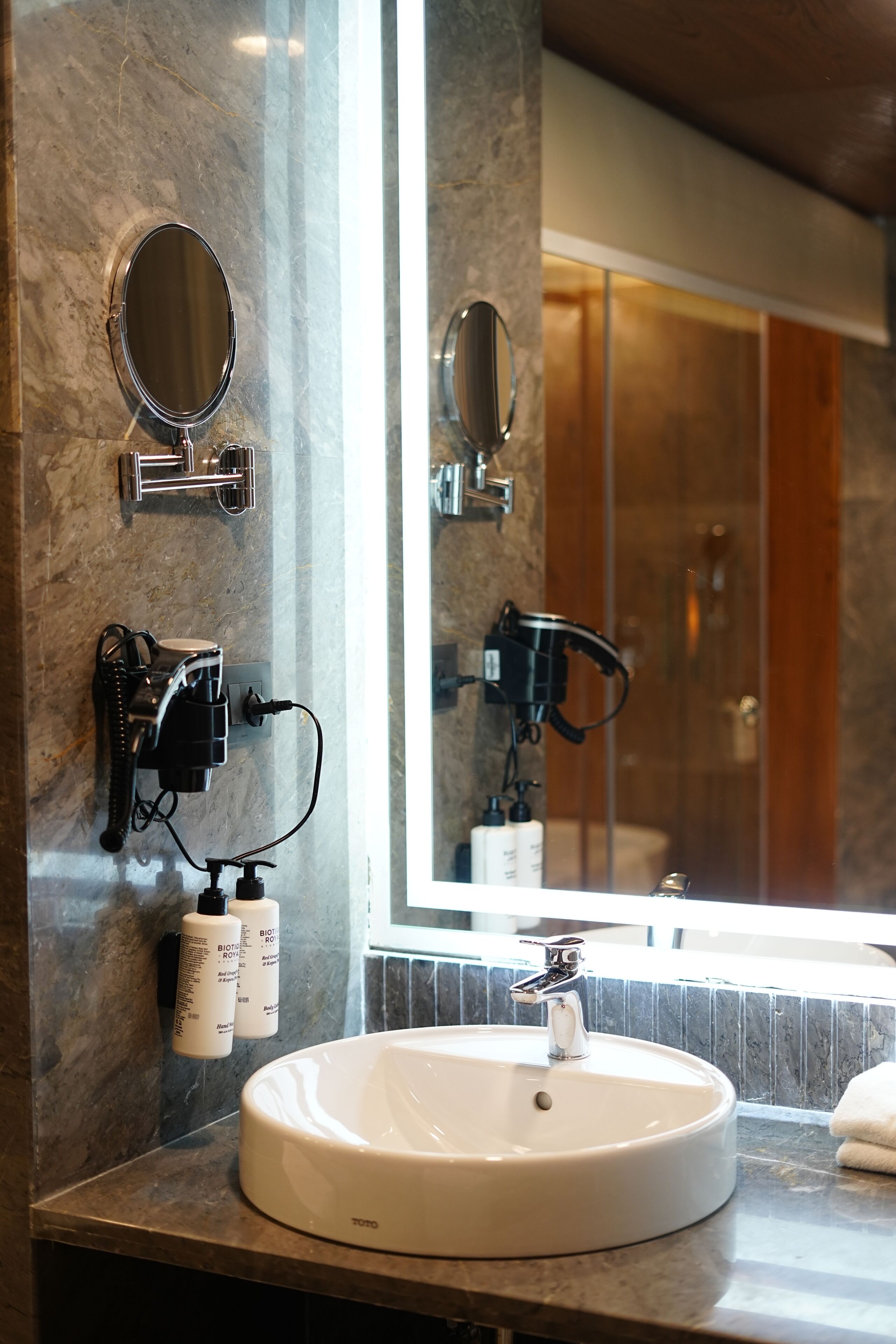 A bathroom with a round white sink, two mirrors, and a large mirror reflecting a shower area.