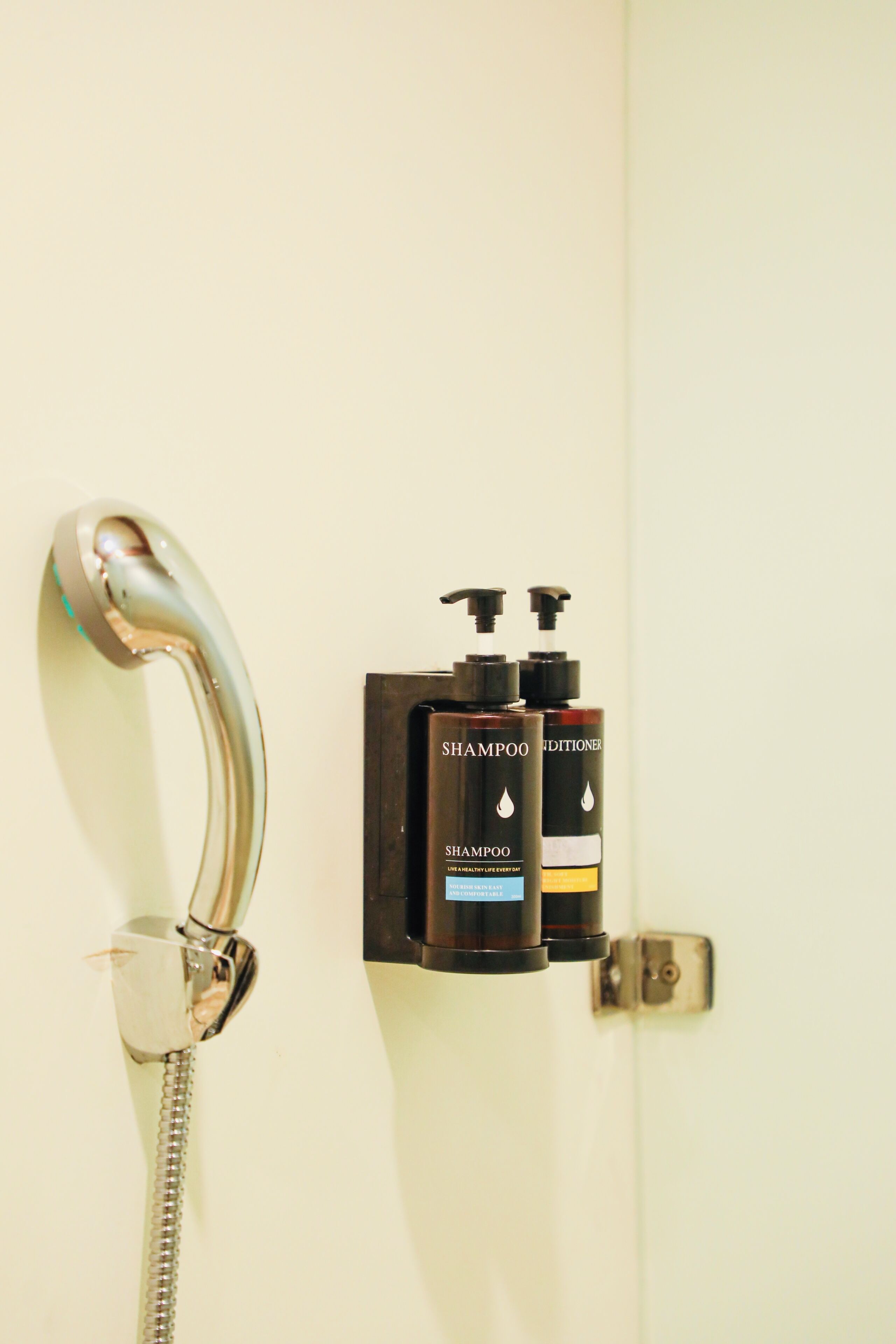 A shower with a modern design, including a curved faucet and a handheld showerhead. There are two bottles of shampoo and conditioner on the wall.