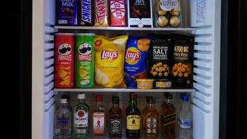 Un refrigerador lleno de diversos alimentos y bebidas, incluyendo aperitivos, bombones y refrescos.