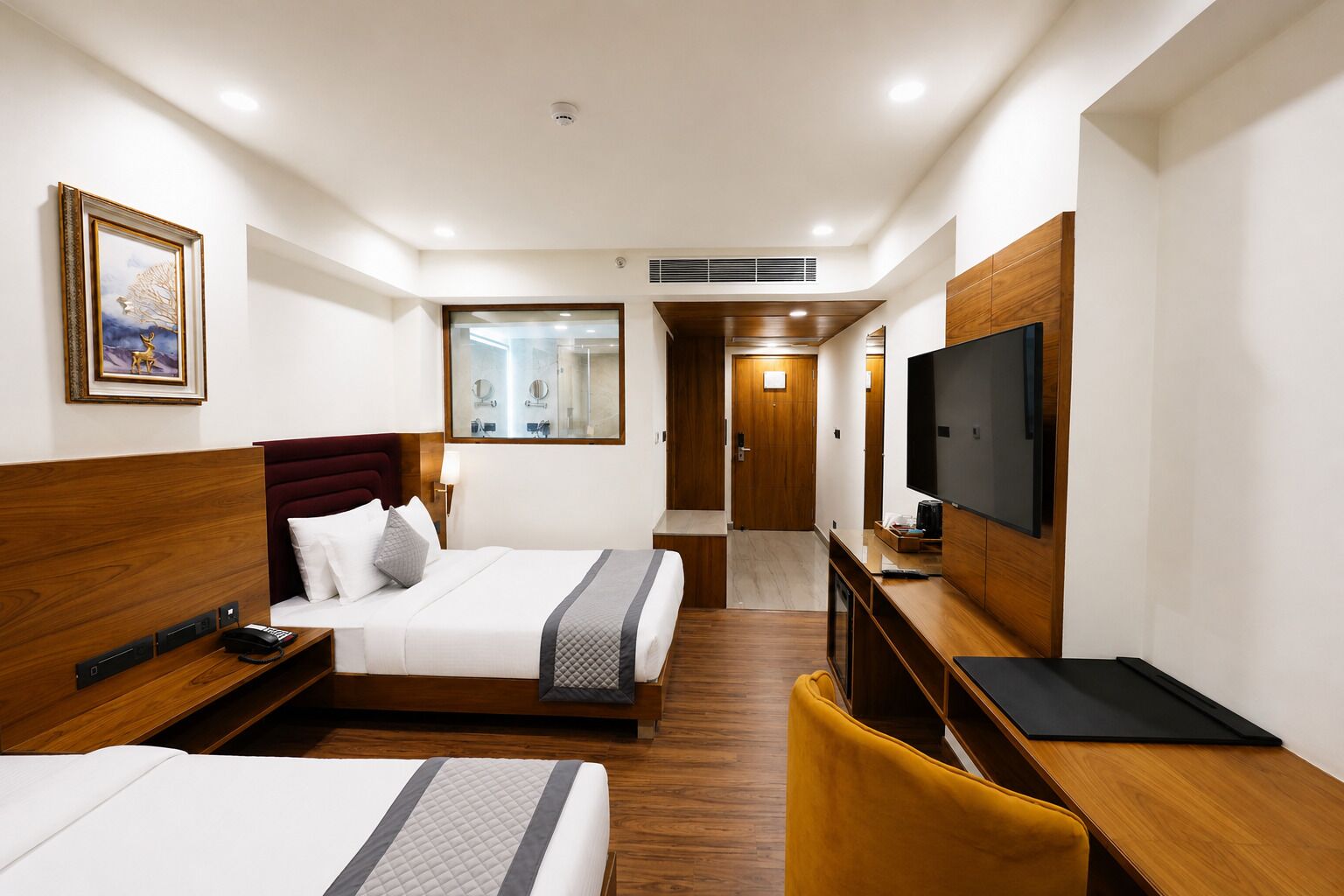 Een hotelkamer met een bed, een bureau, een televisie en een badkamer, zichtbaar door een glazen deur.