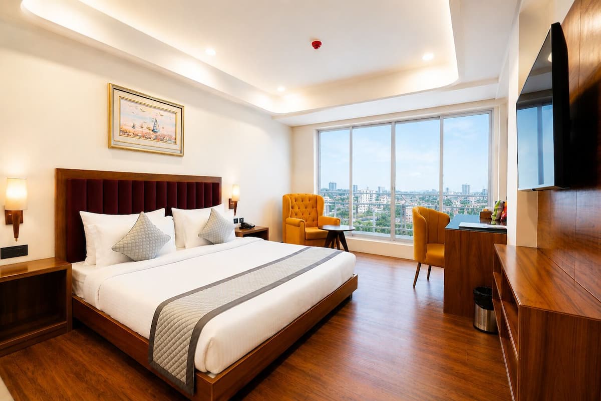 A hotel room with a large bed, a desk, two chairs, a TV, and a city view.