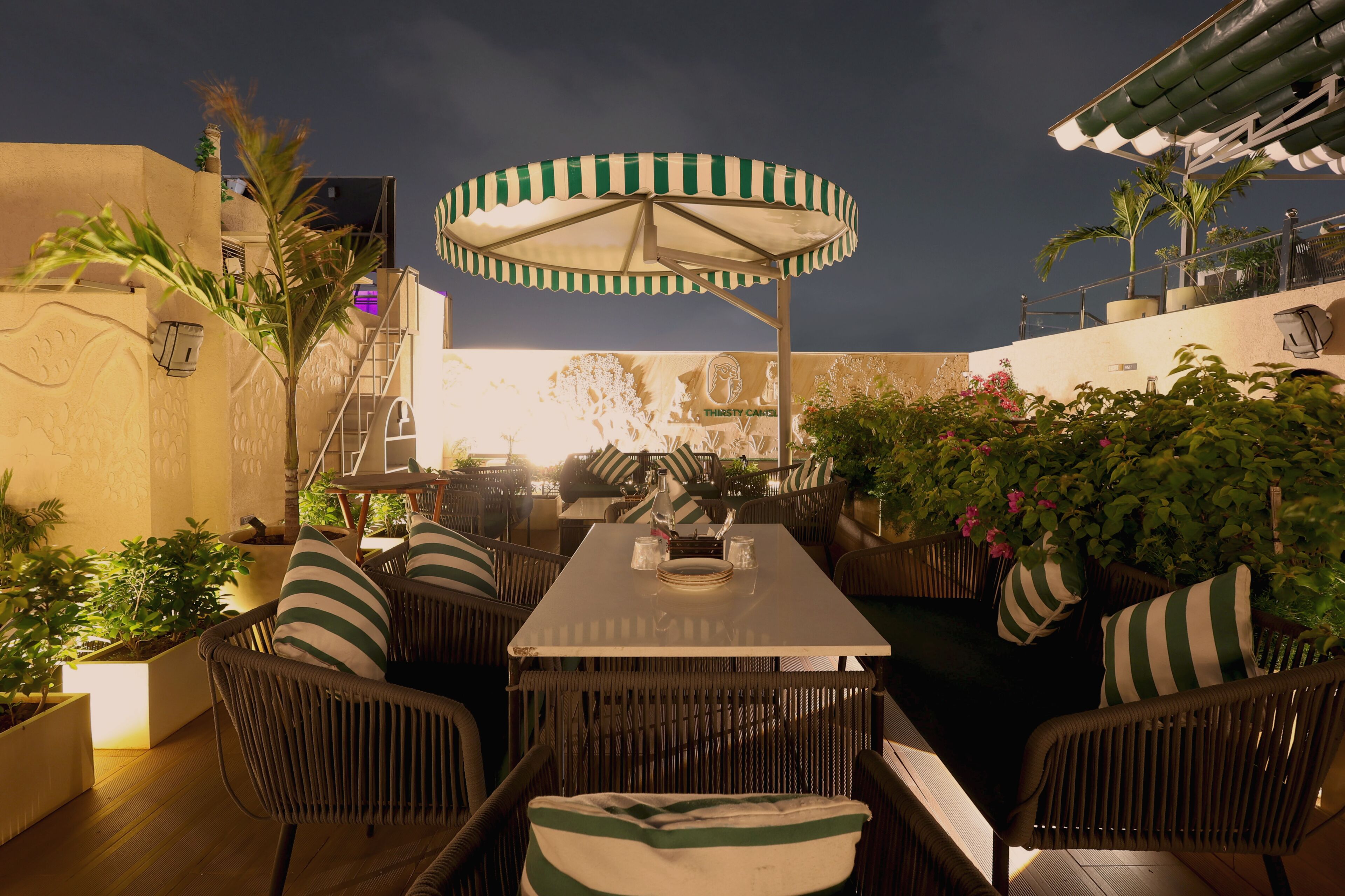 Un espace extérieur aménagé pour les repas, avec des meubles en osier, des coussins à rayures et un parasol à rayures vertes et blanches.