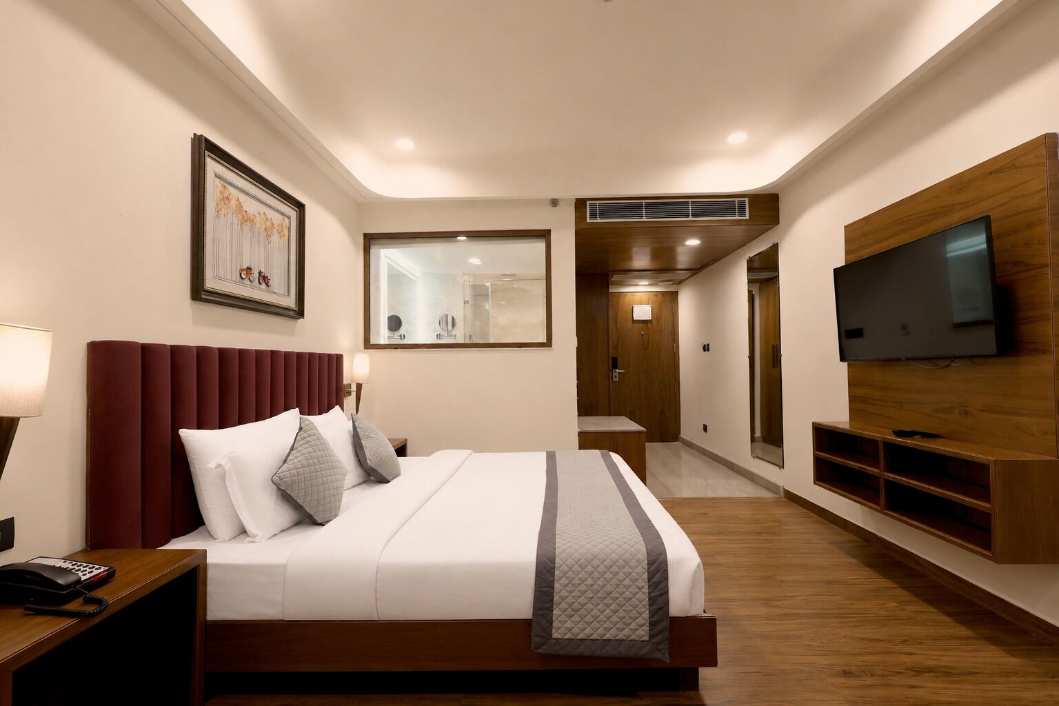 Une chambre d’hôtel moderne, dotée d’un grand lit, d’un téléviseur fixé au mur et d’une salle de bain visible à travers une porte en verre.