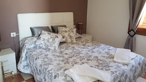 A neatly made bed with floral bedding, a bedside table with a lamp, and a wall-mounted artwork. - Las Belisas (Mercadal)