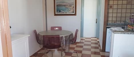 A compact room with a dining table and chairs, a small kitchen area, and a door leading to another room.