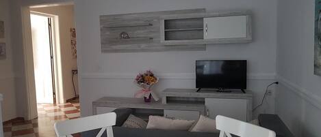 A modern living room with a white round table, grey sofa, and a flat-screen TV on a wooden cabinet.