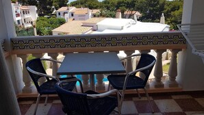 A balcony with a checkered floor, two wicker chairs, and a table. - Las Belisas (Mercadal)