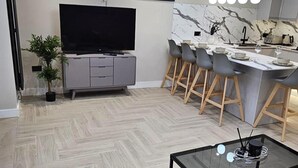 A modern kitchen with a marble backsplash, a dining area with bar stools, and a flat-screen TV on a grey cabinet. - Chester - 4 Bed House Free Parking (Chester)