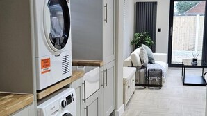 A modern kitchen with a built-in washing machine, a dining area with a table and chairs, and a large window with curtains. - Chester - 4 Bed House Free Parking (Chester)