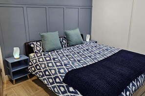 A bedroom with a patterned bedspread, two pillows, a bedside table with a lamp, and a dark blue throw blanket. - Chester - 4 Bed House Free Parking (Chester)