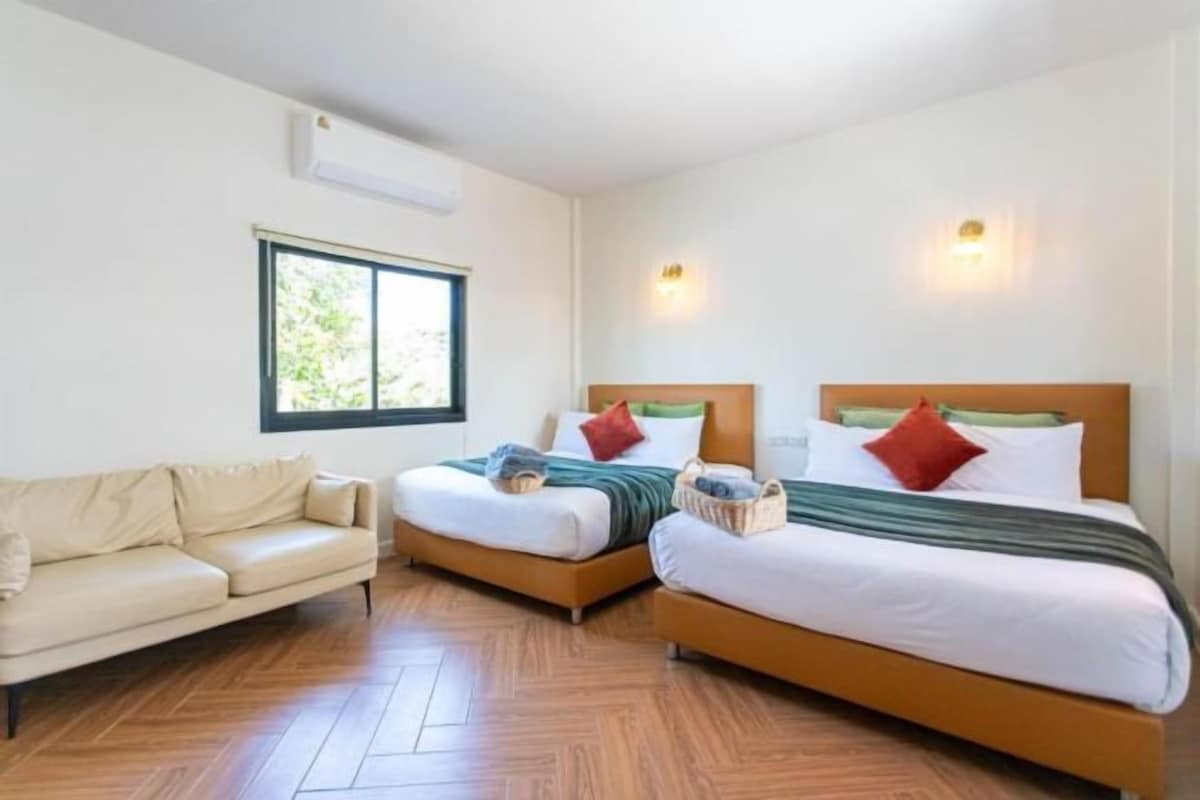 A hotel room with two single beds, a sofa, and a window.