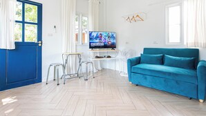 A living room with a blue sofa, a TV, a small table, and a chair. - Vawa Guesthouse (Kanchanaburi)