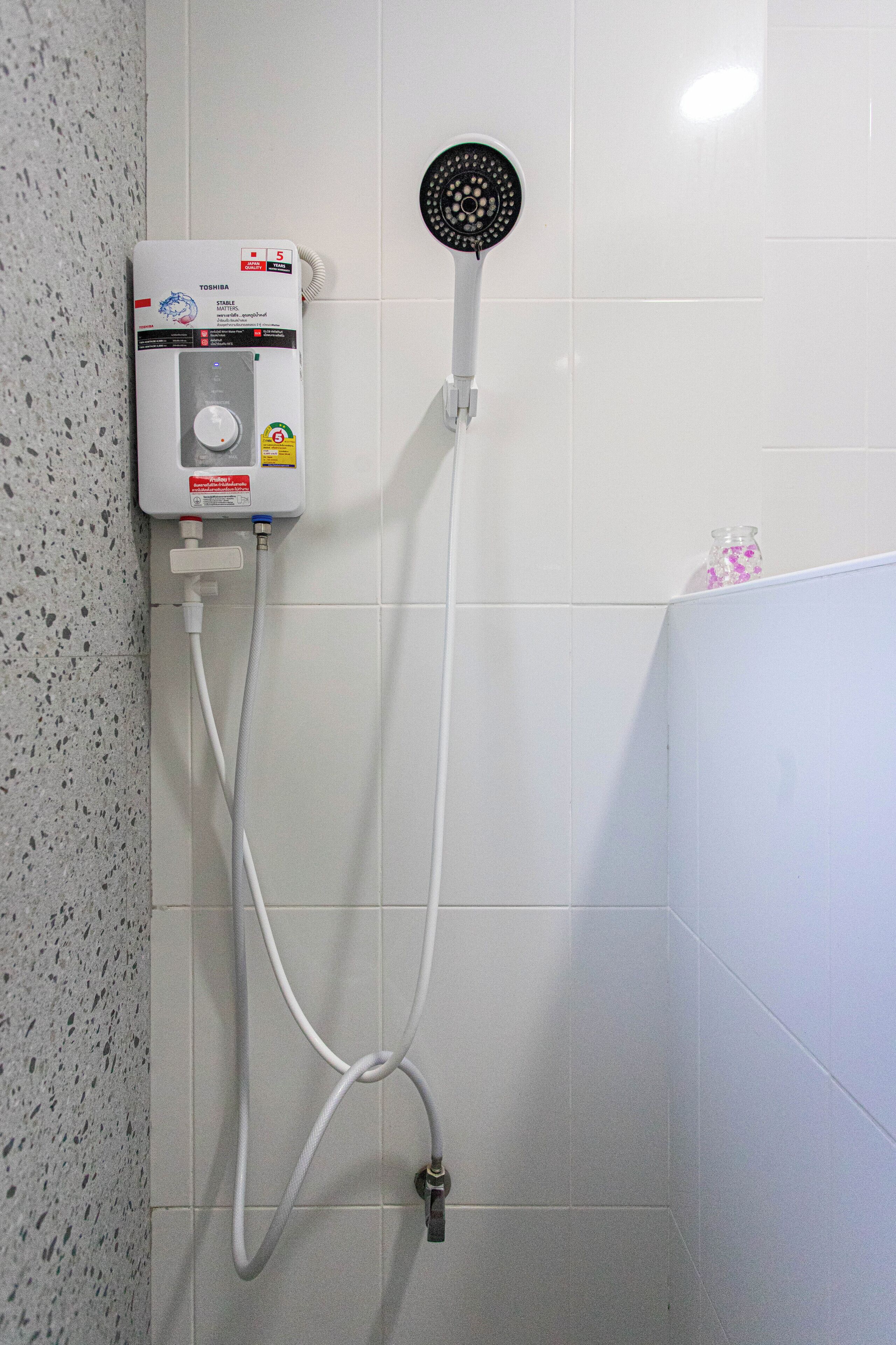 A bathroom with a wall-mounted water heater, a handheld showerhead, and a faucet.