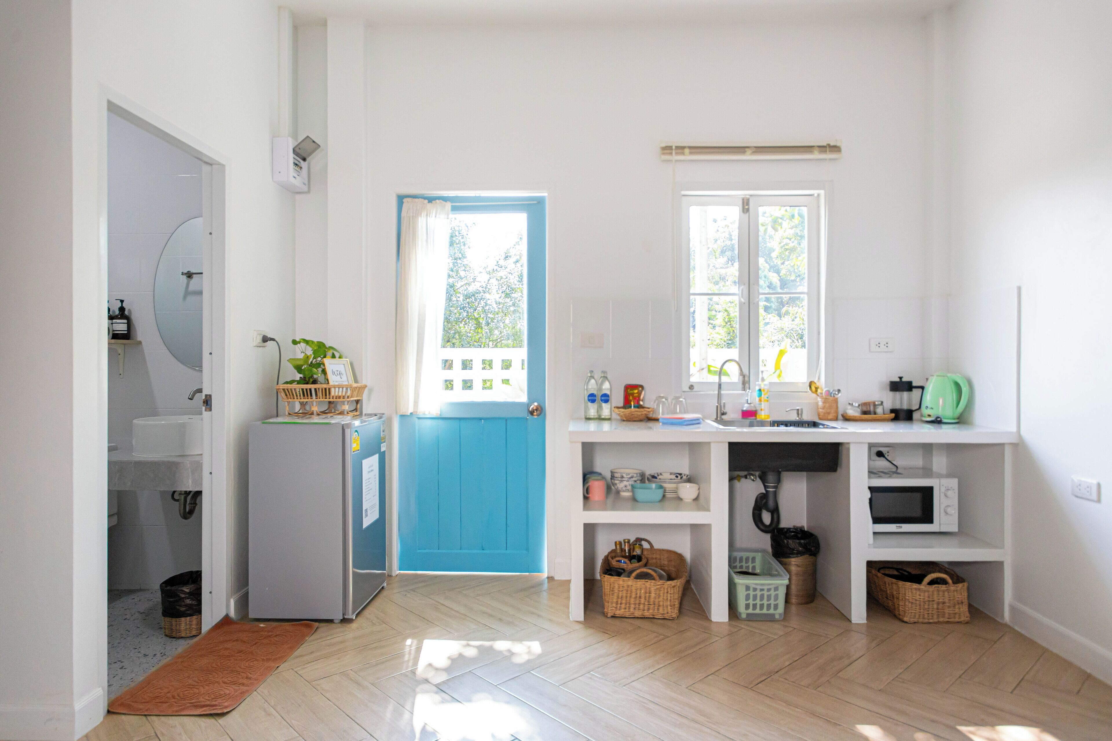 A bright kitchen with a blue door, white cabinets, and a window.
