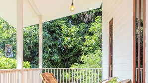 A covered porch with wooden flooring, white railings, and a row of wicker chairs. - Vawa Guesthouse (Kanchanaburi)