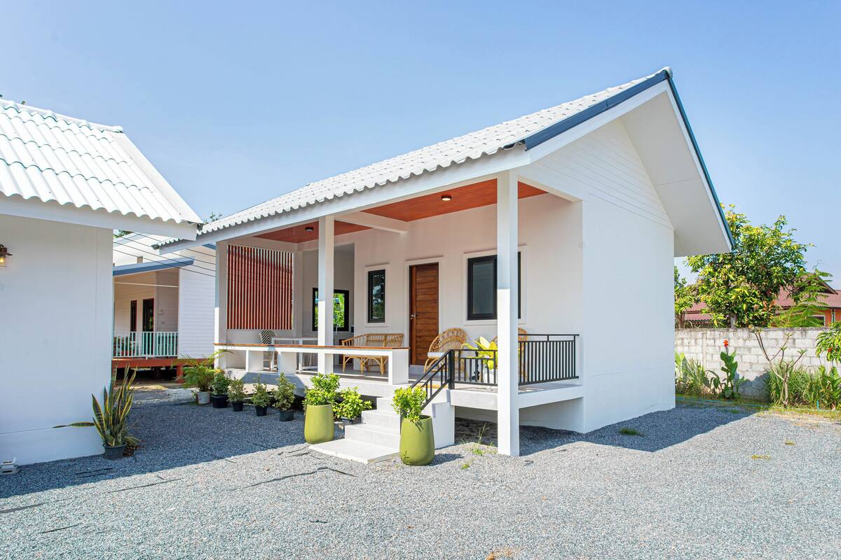 Een modern huis met een overdekte veranda, een houten terras en een kleine tuin met potplanten.