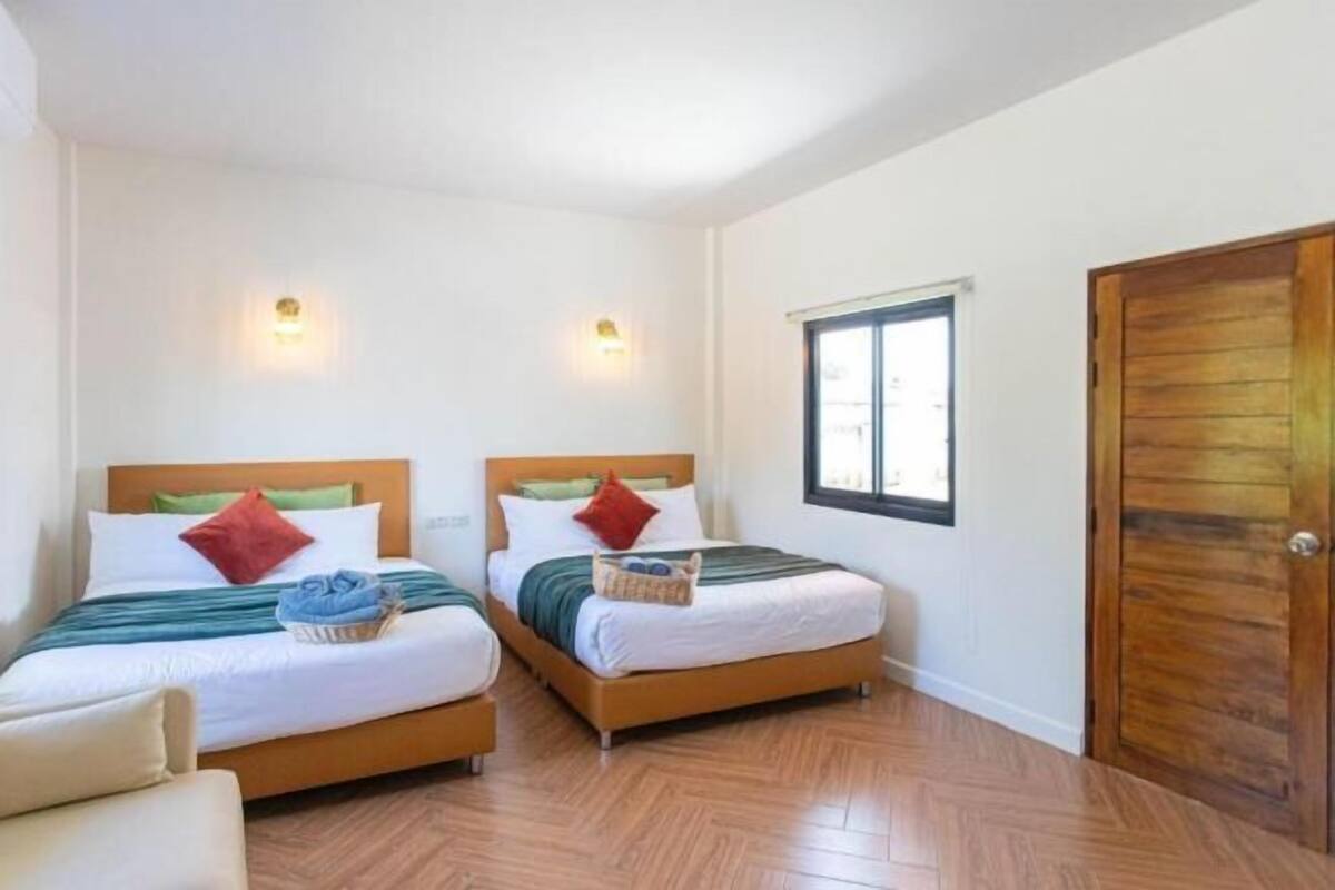Een hotelkamer met twee bedden, houten hoofdeinden, witte wanden en een houten deur.