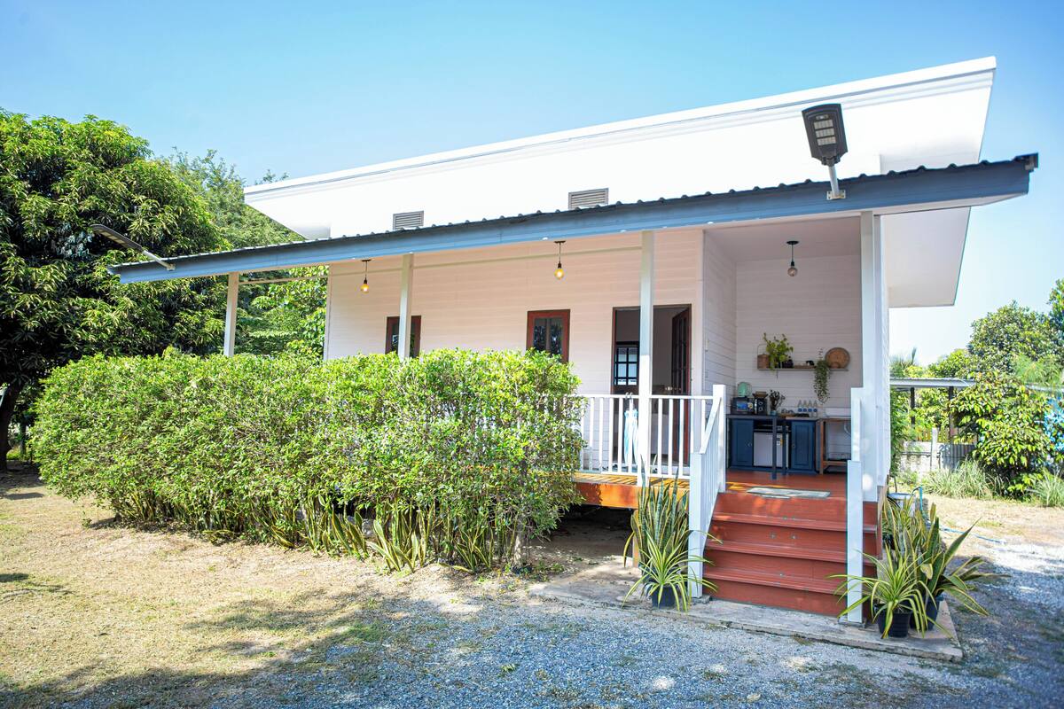 Een wit huis met een overdekte veranda, een keuken en een oprit met grind.