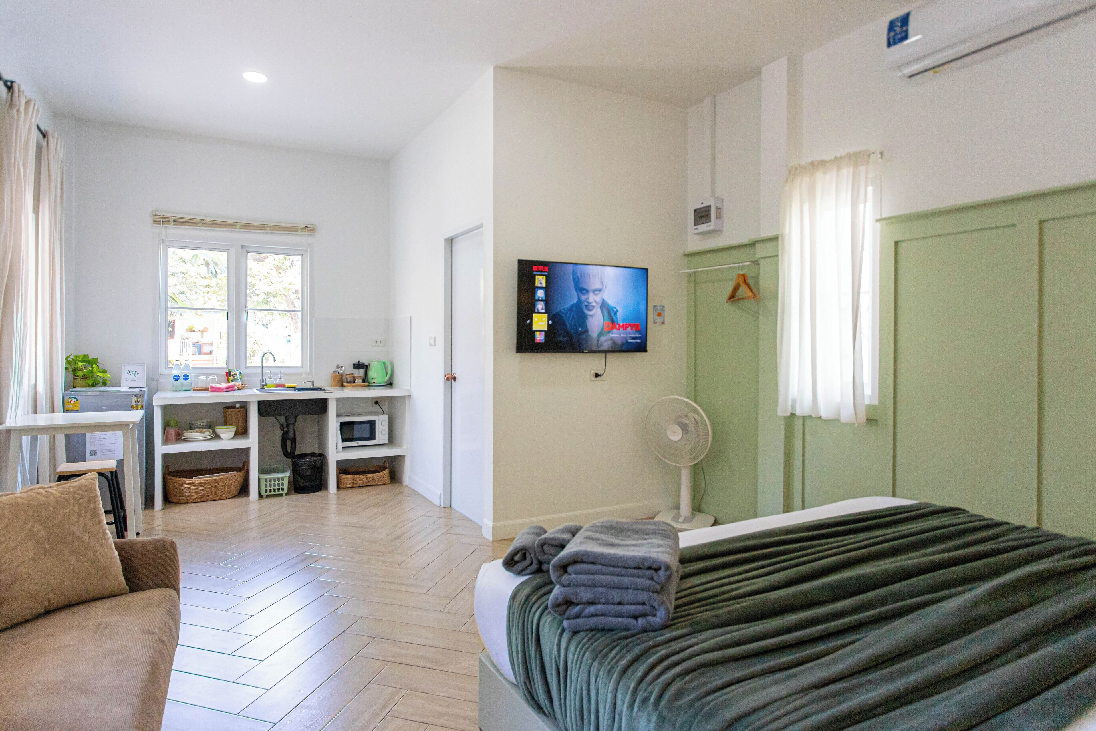 Habitación de hotel con cama, televisor montado en la pared, escritorio con computadora y ventana con cortinas.
