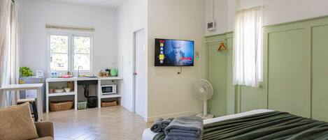 Habitación de hotel con cama, televisor montado en la pared, escritorio con computadora y ventana con cortinas.