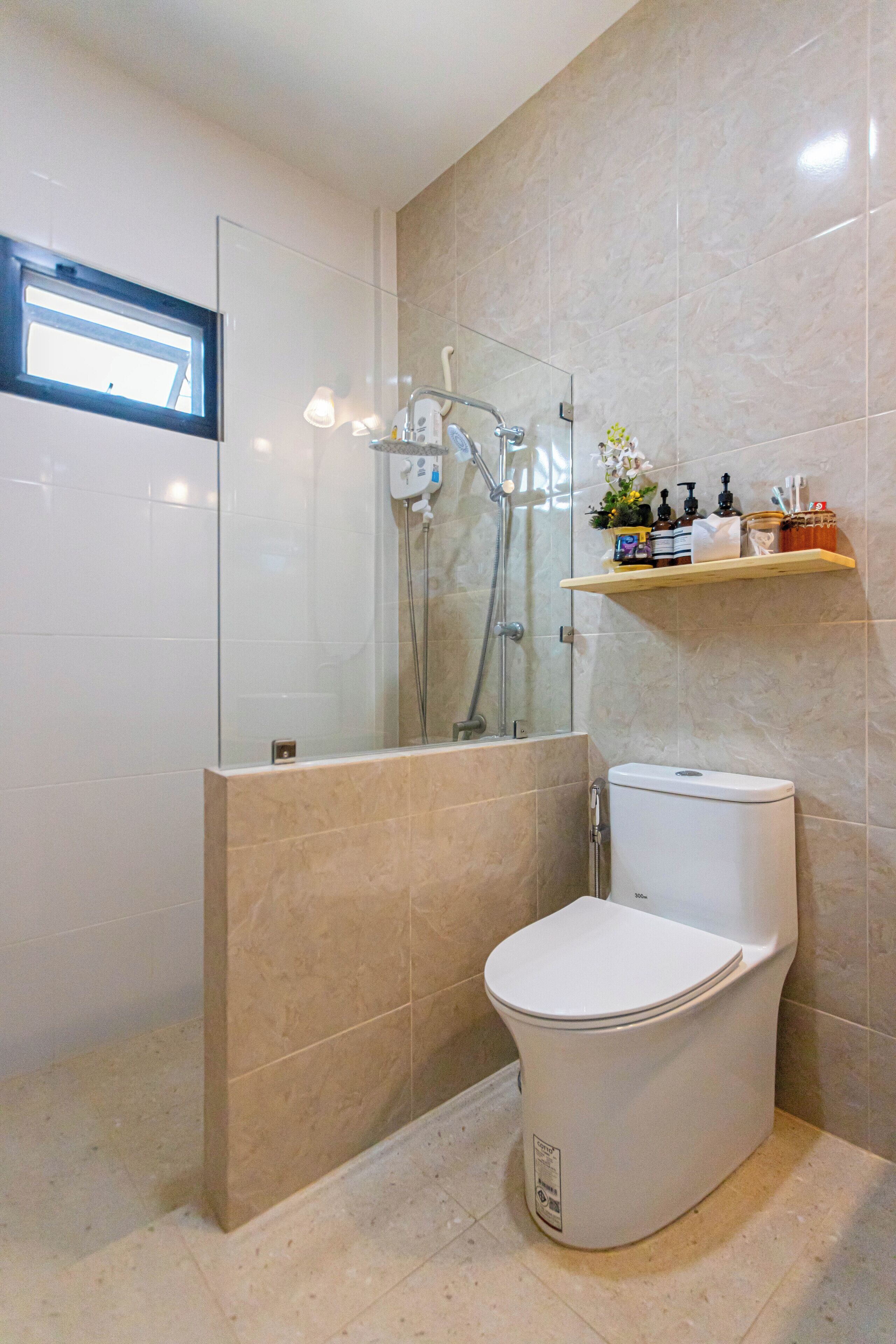 Un baño moderno con ducha de vidrio, inodoro y estante con artículos de aseo.