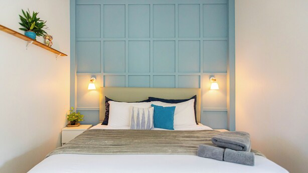 A neatly made bed with a white and gray striped blanket, a blue pillow, and two folded towels. - Vawa Guesthouse (Kanchanaburi)