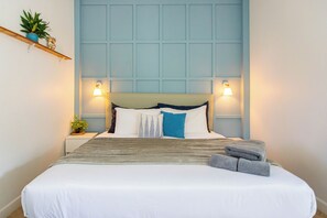 Ein ordentlich gemachtes Bett mit einer weiß-grauen Streifenauflage, einem blauen Kopfkissen und zwei gefalteten Handtüchern.