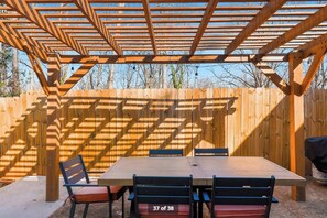 Une terrasse extérieure couverte, avec une table et des chaises en bois, une pergola en bois et une clôture en bois en arrière-plan.