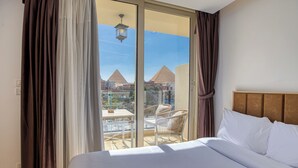 Habitación de hotel con una cama grande, vistas a las pirámides a través de una puerta de cristal y un balcón con sillas.