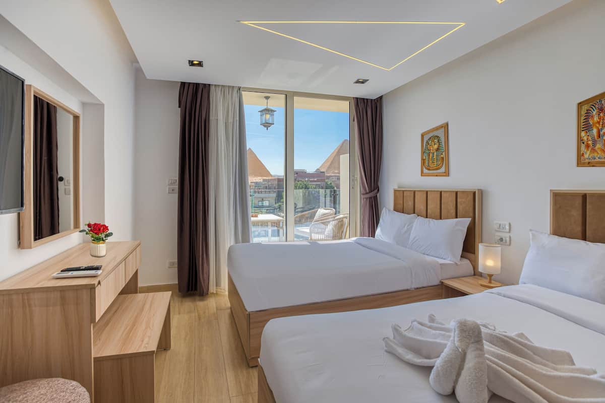 Habitación de hotel con dos camas, un escritorio, una silla y vista a las pirámides.
