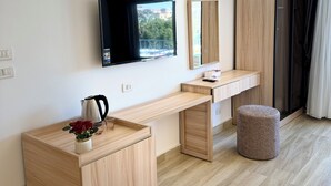 Habitación de hotel moderna con un escritorio de madera, un televisor de pantalla plana montado en la pared, un taburete pequeño y una ventana con vistas a edificios.