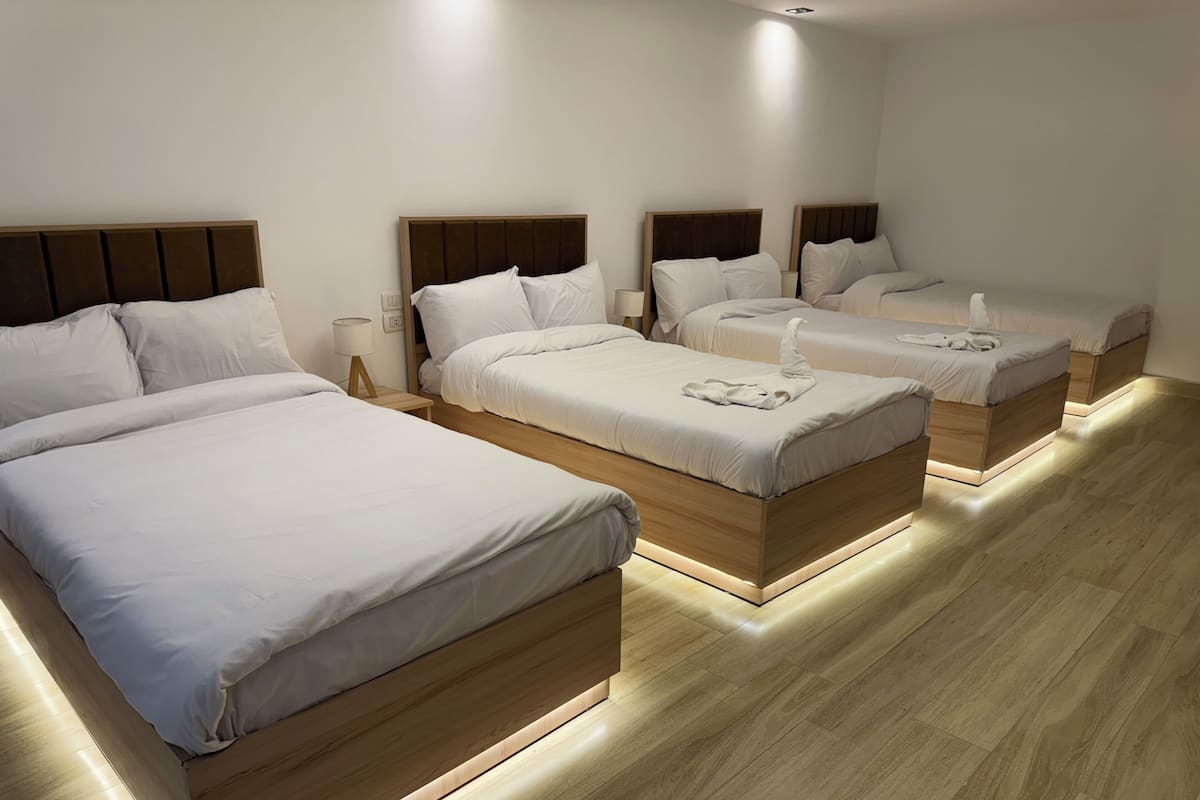 Habitación de hotel con tres camas, cada una con cabeceros de madera y ropa de cama blanca.