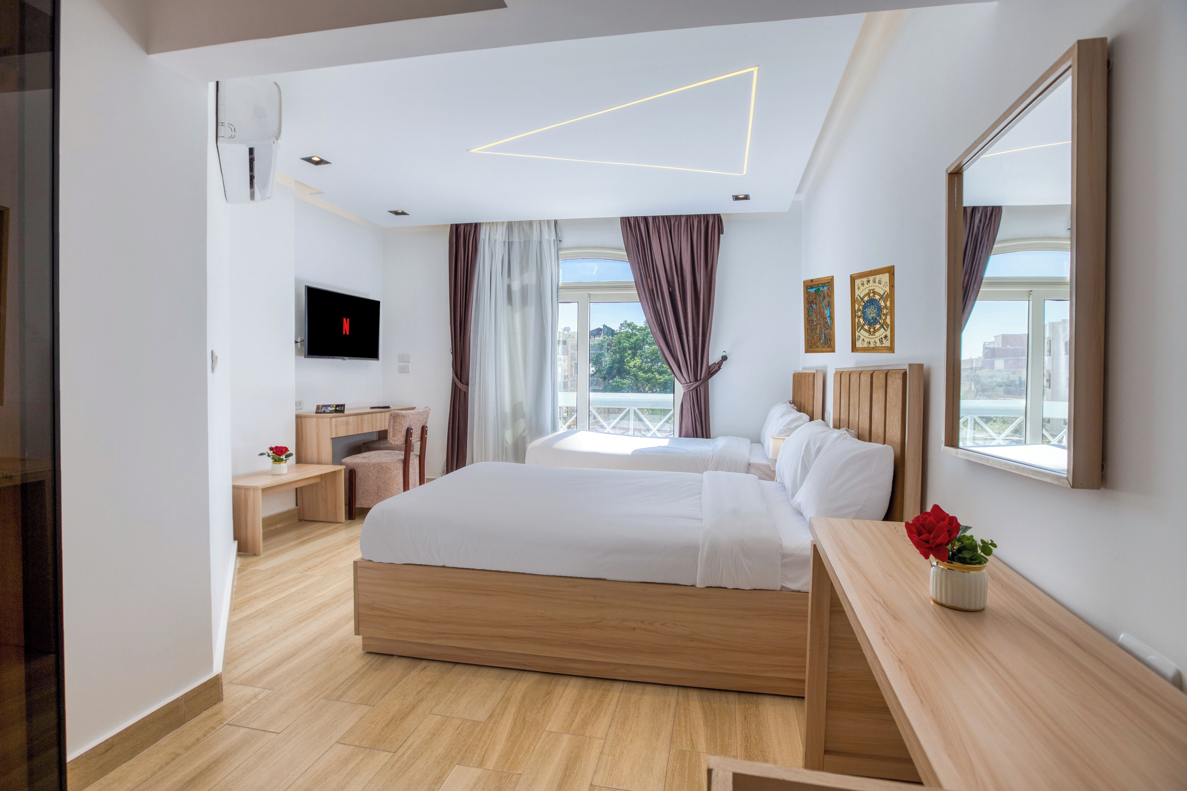 A modern hotel room with a large bed, a desk, a TV, and a balcony view.