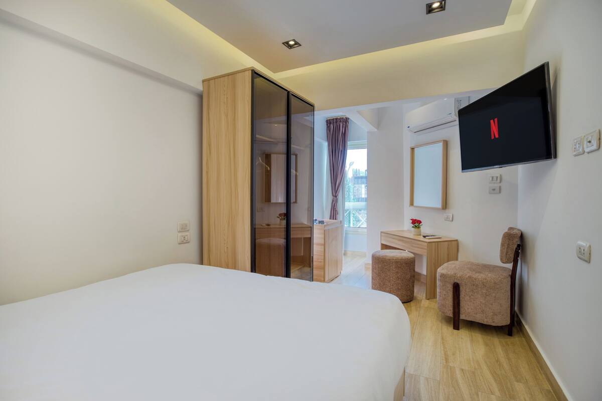 Una habitación de hotel moderna con una cama grande, un escritorio, una silla y un televisor fijado a la pared.