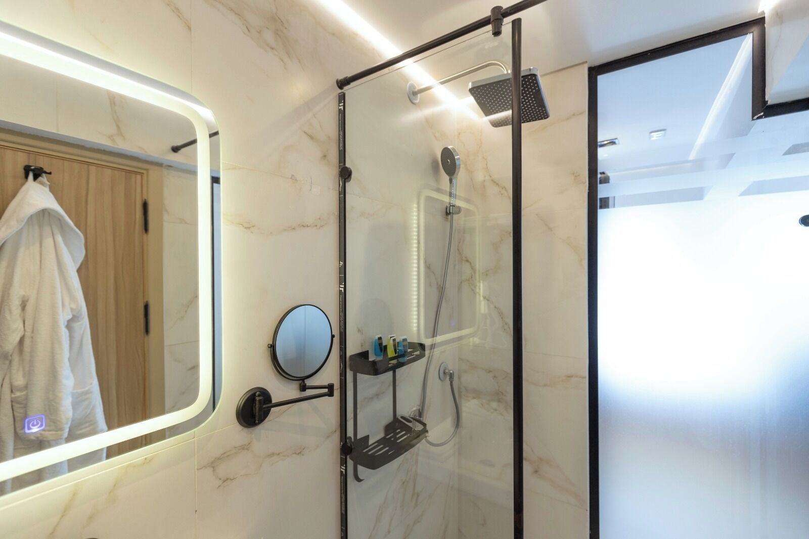 Un baño moderno con ducha envuelta en vidrio, un espejo redondo y un perchero para toallas.