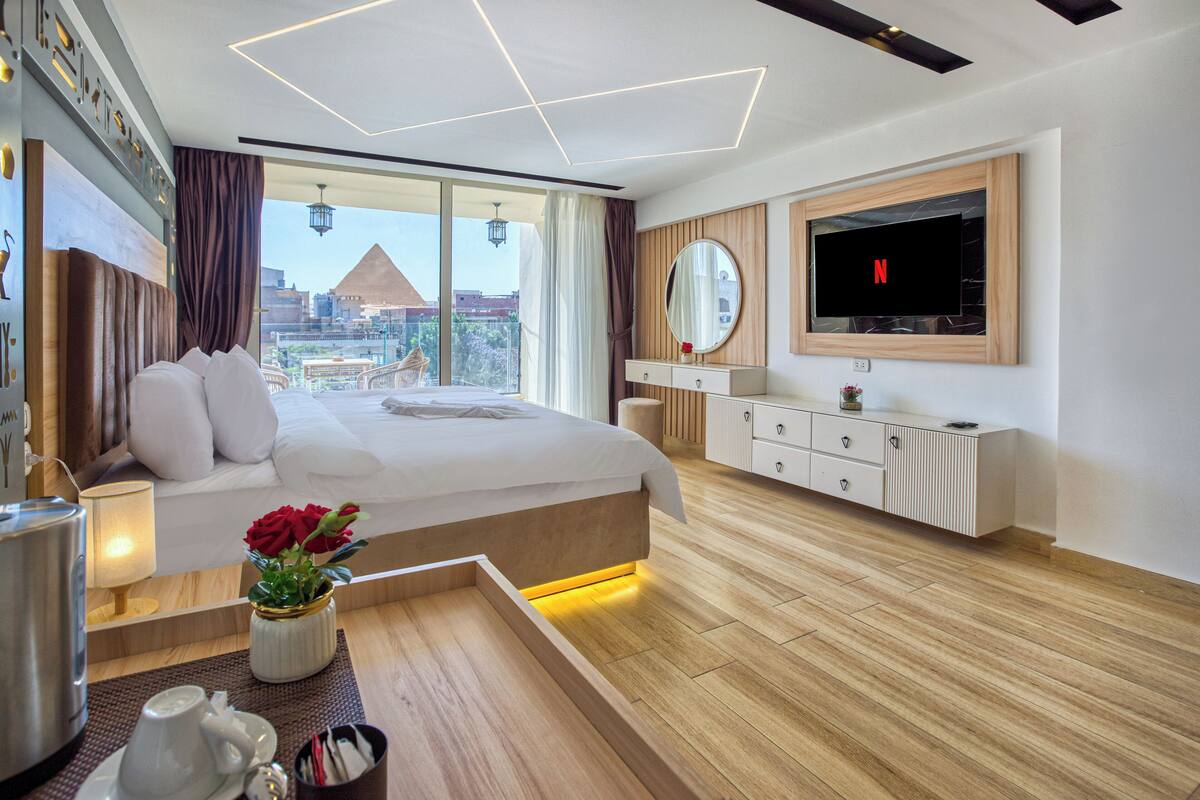 Habitación de hotel moderna con una cama grande, un televisor montado en la pared y vistas a un paisaje urbano.