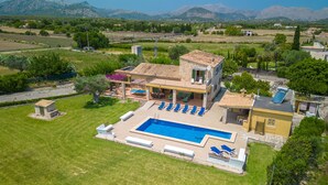 A large house with a swimming pool, a patio with lounge chairs, and a view of mountains.