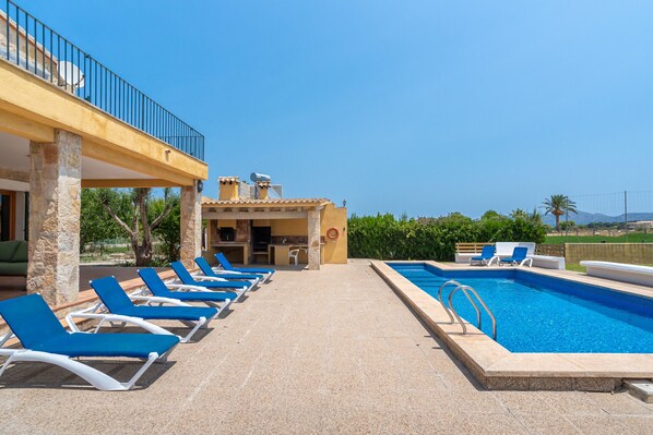 A pool area with blue lounge chairs, a clear sky, and a view of the landscape.
