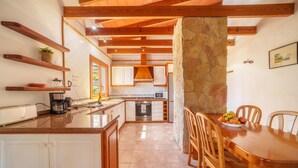 A kitchen with wooden beams, white cabinets, a stone column, and a dining table with chairs.