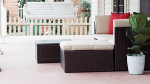 A covered porch with wicker furniture, a white bench, and a potted plant.