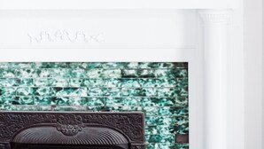 A white fireplace mantel with a TV above it, decorative candles, a teapot, and two potted plants.