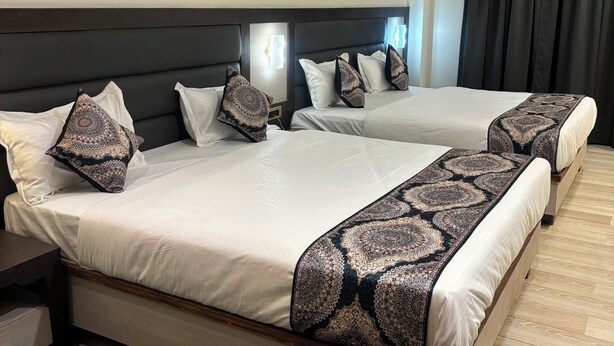 A hotel room with two beds, dark headboards, and a ceiling fan. - Hotel Gurudev Kunj (Faizabad)