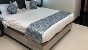 A neatly made bed with a patterned bedspread, a dark headboard, and a ceiling fan. - Hotel Gurudev Kunj (Faizabad)