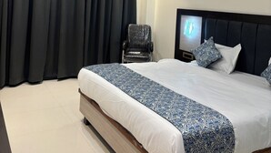 A hotel room with a large bed, a chair, a ceiling fan, and a night light on the headboard. - Hotel Gurudev Kunj (Faizabad)