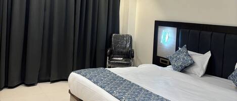 Ett hotellrum med en stor säng, en stol, en takfläkt och en nattlampa på sänggaveln.