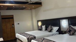 A hotel room with two beds, a ceiling fan, a wooden wardrobe, and a small desk with a lamp. - Hotel Gurudev Kunj (Faizabad)