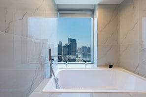Une salle de bain moderne dotée d’une grande baignoire, d’une douche à parois de verre et offrant une vue sur la ville grâce à une grande fenêtre.
