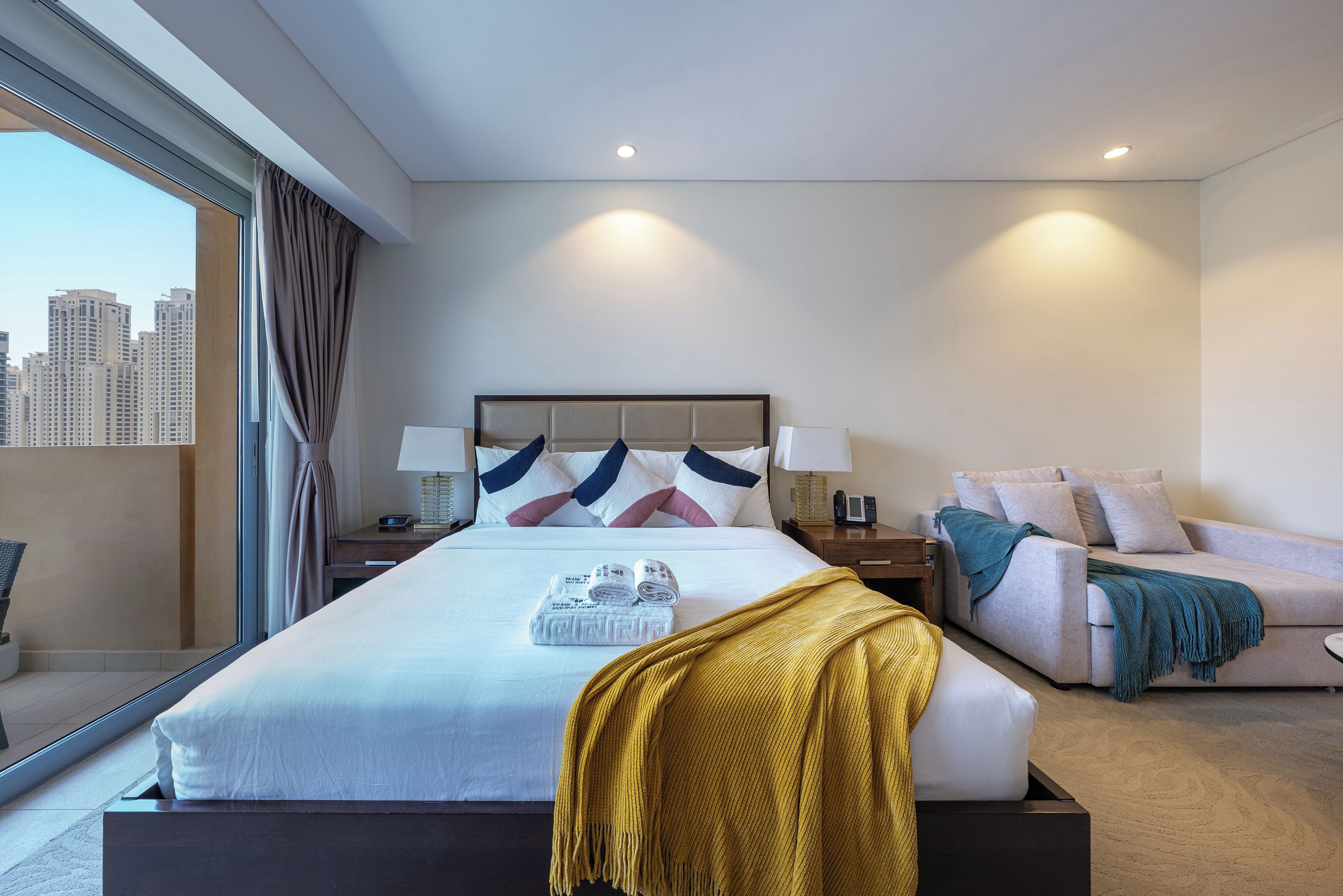 Une chambre d’hôtel avec un grand lit, un canapé, une fenêtre avec des rideaux et une vue sur la ville.